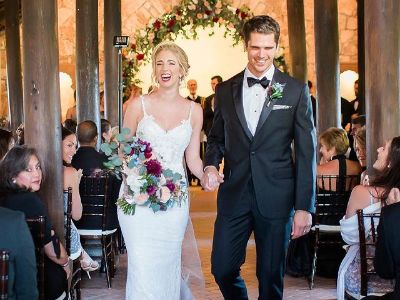 Brian Shimansky and Brit Shimansky are walking past the people as Brit is holding flowers in her hand.